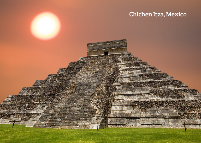 Ancient Mayan ruin of Chichen Itza with the sun glowing in an orange sky